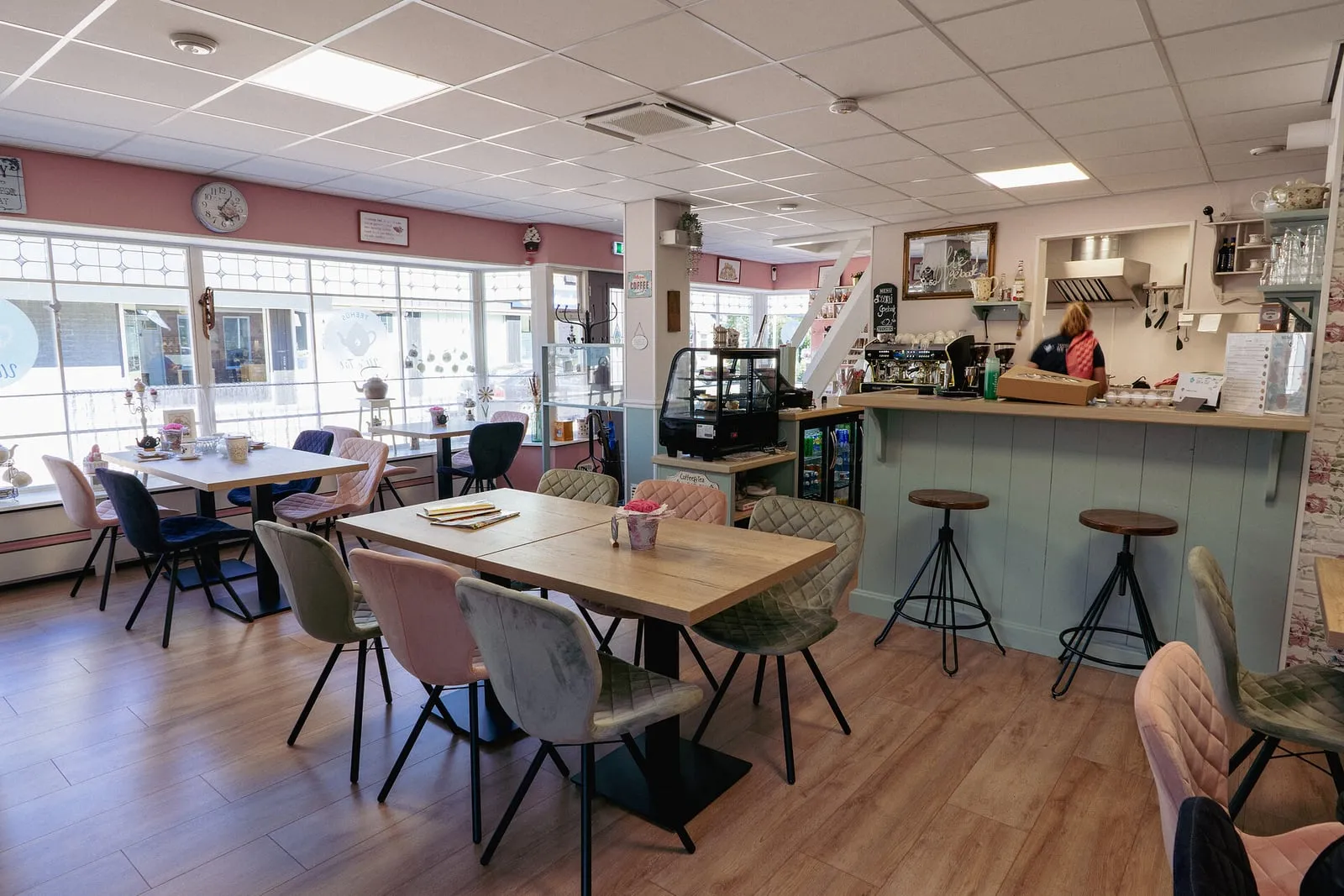 Het interieur van het teehûs: houten tafels, roze en grijze stoelen en de bar met vitrine.